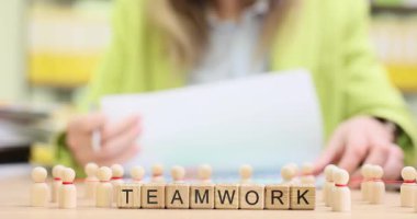 Kadın takım çalışması ve masa başında personeli gösteren küçük tahta heykelciklerle blokların yakınındaki kağıtları gözden geçiriyor. Takım çalışması odaklı ortamlarda ortak çaba