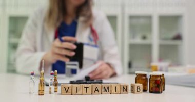 Kadın doktor, masa başında, tahta bloklarda B vitamini ile damga basıyor. Yavaş çekimde vitaminleri içeren besin takviyelerine odaklanın