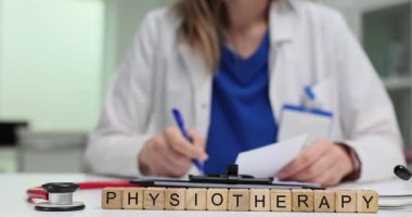 Fizyoterapi yakınında masa başındaki tahta bloklarda evraklarla ilgilenen bir tıp uzmanı. Klinikte fizyoterapinin idari ve pratik yönleri