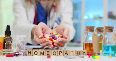 Kadın Homeopati 'nin yakınında bir avuç renkli kapsül tutuyor ve etrafa saçılmış haplarla şişeler tutuyor. Alternatif tıp ve ilgili ilaçlar