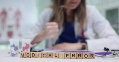 Profesyonel kadın sıkıntılı ve kızgın bir şekilde tahta bloklarda tıbbi hatalar masasında oturuyor. Yerçekimi ve etkisi sağlık hizmetlerindeki hatalarla ilişkilidir