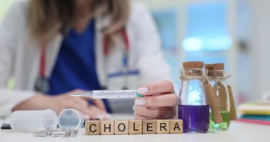 Kadın termometreyi kolera ve renkli reaksiyonlu şişelerle blokların yakınında tutuyor. Modern klinik ortamlarda koleranın teşhisi ve yönetimi
