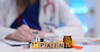 Tahta küplerin yanında ağrı kesici şişesi ve şırınga bulunur. Kadın doktor reçeteli ilaç yazıp ağrı kesici sorununu ciddi olarak çözüyor.