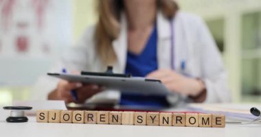 Tahta küpler steteskop ve panonun yanına yerleştirilmiş Sjogren Sendromu 'nu büyülüyor. Kadın doktor, otoimmün hastalıklar üzerine çalışan hasta verilerini derinden inceliyor.