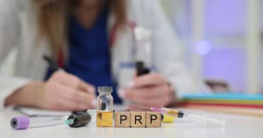 Tahta küplere yazılan PRP kelimesi şişelerle dolu şırıngaların arasında duruyor. Kadın doktor trombosit zengini plazma terapisi hakkında tıbbi notlar yazıyor.