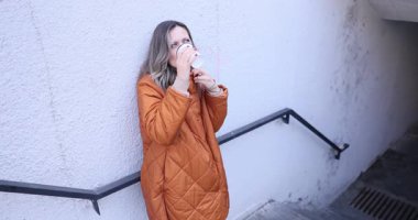 Turuncu montlu kadın, merdivenlerden inen yeraltı merdivenlerinde tek başına kahveden hoşlanıyor. Sabah ışığı ve huzurlu ifade yavaş bir duraksama hissi yaratır.