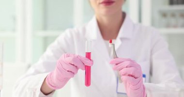 Kadın laboratuar teknisyeni kapsülü cımbız ve test tüpüyle dikkatlice tutuyor. Paltolu kimyager tablet bileşiminin analizi için hazırlanıyor. Yavaş çekim