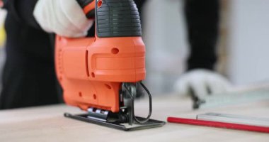 Deneyimli bir inşaat işçisi, tahta kalas boyunca elektrikli yapboza rehberlik eder. İnsan kenarı pürüzsüz ve dengeli kılmak için kalasları kontrol eder. Yavaş çekim