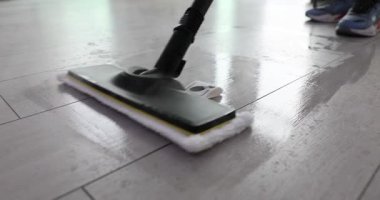 Spor ayakkabılı adam, kaplamaları temizlemek için buharlı paspası ileri geri hareket ettiriyor. Mikrofiber paspas tozu ve yapışkan lekeler topluyor. Yavaş çekim