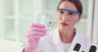 Kadın kimyager laboratuardaki Petri kabının içeriğini dikkatlice inceliyor. Deneyimli laboratuvar teknisyeni materyalde gözle görülür değişiklikler gözlemler. Yavaş çekim