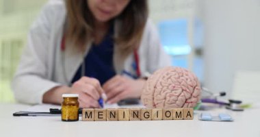 Yapay beyin modelinin önüne konulan bloklardan oluşan menenjiyom harfleri. Kadın doktor, beyaz masaüstündeki tümör vakası üzerinde çalışıyor.