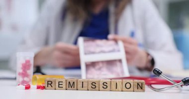 Remisyon, açık derginin yanındaki tahta küplerde ve masadaki haplarda görülür. Doktor, hasta geçmişini ve iyileşme aşamasını yansıtan ultrason fotoğrafını inceliyor.