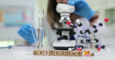 Küpler tarafından oluşturulan oksikodon kelimesi mikroskop ve molekülün yanında duruyor. Kadın teknisyen madde formunu ölçen kimyasal bağ yapısını araştırıyor.