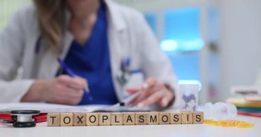 Tahta küplerden yapılmış Toksoplazmoz kelimesi masanın ortasında duruyor. Hasta teşhisi için hazırlanmış araçlarla kadın tıbbi çalışmalar