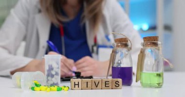 Tahta bloklar, kapsüllerin ve renkli sıvıların yanında kalarak Hives kelimesinin hecelenmesini sağlar. Doktor alerji reaksiyonlarını araştıran notlar yazar ve arı kovanı tedavisi yapar.