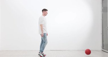 Sporcu parlak odanın zemininde ritmik olarak turuncu basketbolu zıplatır. Kot pantolonlu sportif erkek sürüş antrenmanlarını tekrarlıyor. Yavaş çekim