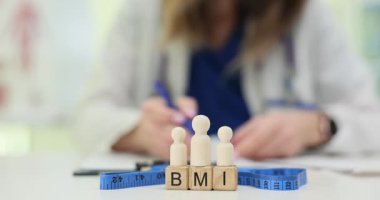 Tahta bloklar BMI 'nin not defterinde yazan doktorun yanında vücut kitle indeksini açıkladığını gösteriyor. Tablonun üzerindeki ağırlık kontrolünü gösteren figür ve mezuralar