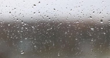 Şeffaf yağmur damlaları pencerenin tüm cam yüzeyini kaplar. Yağmur damlaları pencereden süzülüp uzun ıslak izler bırakıyor. Cam sisli görünüyor