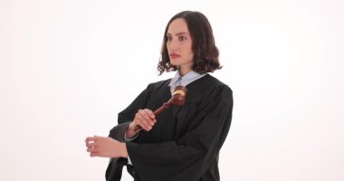 Kadın yargıç kollarını göğsünün önünde beyaz arka planda tahta tokmakla çapraz bağlar. Dişi, dik dik bakıyor, ciddi bir yüz ifadesiyle yargılayarak.