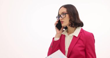 İş kadını evrakları elinde tutuyor ve beyaz arka planla ilgili görüşmeler sırasında telefonla konuşuyor. Kadın ofiste önemli konuları tartışıyor.