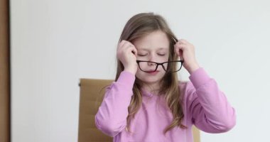 Pembe kapüşonlu şirin kız masasında otururken gözlük takıyor. Görme engelli liseli kız yavaş çekimde çalışmak için gözlük kullanıyor.