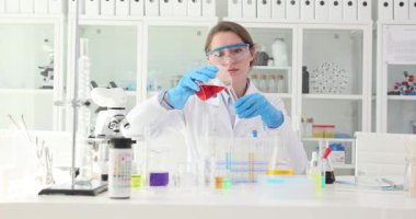 Kadın bilim adamı laboratuarda test tüpüne kırmızı reaktif solüsyon koyuyor. Araştırmacı reaksiyonu gözlemler ve verileri dikkatli bir şekilde tutar.