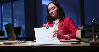 İş kadını video konferansı sırasında masada oturuyor ve ekranda ortağını göstermek için grafiklerle birlikte yazılı belge tutuyor. Kadın çevrimiçi toplantı düzenliyor