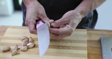 Erkek şef mutfak tezgahında keskin bir bıçakla sarımsak karanfillerini dikkatlice soyar. Profesyonel aşçı sarımsak karanfilinden ince deriyi temizler. Yavaş çekim