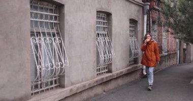 Şık bir sonbahar kıyafeti giymiş kadın şehir caddesinde yürüyor ve taze pişmiş çörek yiyor. Dişi, kaldırımda yürürken yumuşak çörekleri sever. Yavaş çekim