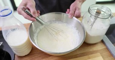 Ev aşçısı hamuru metal kasede çırpar ve pürüzsüz bir dokuyu korur. Ev hanımı fırıncı şişeden süt, cam kavanozdan un kenarları çırpar.