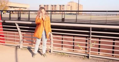 Kadın telefonda konuşurken yaya köprüsünde yürür. Arayan elini sallıyor ve ağır çekimde haberlere yüksek sesle tepki veriyor.