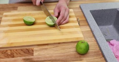 Kadın elleri, tahta kesme tahtasındaki keskin bıçakla limonu dilimlere ayırıyor. Ev hanımı mutfaktaki kokteyller için egzotik malzemeler hazırlıyor.
