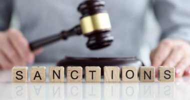 Genç adam elinde yargıç tokmağıyla masada oturuyor. Sıraya dizilmiş minyatür tahta küpler ofis masasında sözcük yaptırımları oluşturur