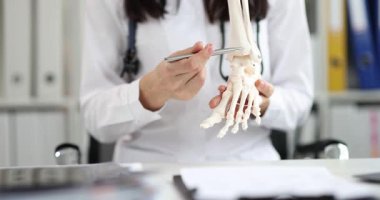 Beyaz laboratuvar önlüklü kadın doktor anatomik ayak iskeleti modelini elinde tutuyor. Deneyimli doktor kemik ve tendonların yapısını açıklıyor