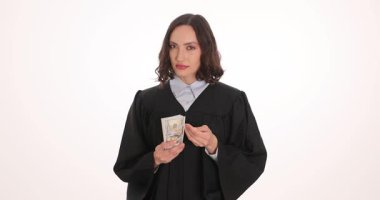 Kadın yargıç, siyah bornozun geniş kolunda rüşvet olarak aldığı bir tomar doları saklıyor. Kadın, adli kıyafetin içine gizlice para sokuyor. Yavaş çekim