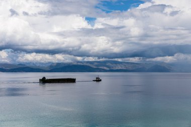 Yunanistan 'daki Korfu adası yakınlarındaki İyon Denizi. Düz bir su yüzeyinde seyreden bir gemi. Güzel kalın bulutlar.