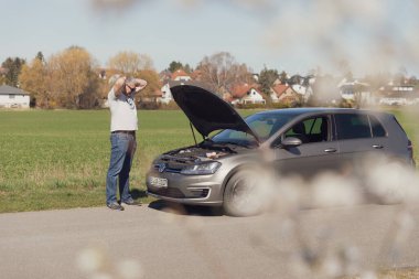 Sürücü arabanın önünde duruyor ve nasıl tamir edileceğini bilmiyor.