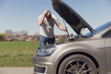 Sürücü arabanın önünde duruyor ve nasıl tamir edileceğini bilmiyor.