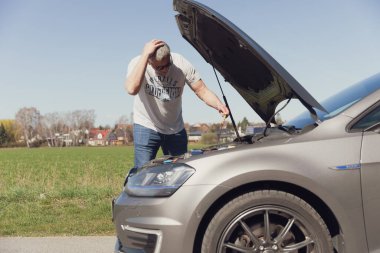 Sürücü arabanın önünde duruyor ve nasıl tamir edileceğini bilmiyor.