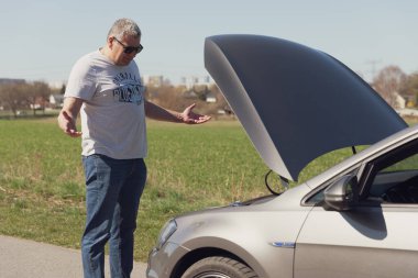 Sürücü arabanın önünde duruyor ve nasıl tamir edileceğini bilmiyor.