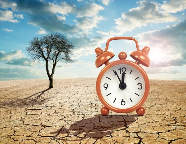 Alarm clock with five minutes before twelve o\'clock on arid cracked soil. Concept of climate change or global warming.