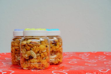 Cornflakes in a plastic jar on a red heart-pattern tablecloth.