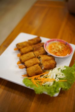 Shrimp spring rolls with pickled vegetables and fresh vegetables on a white plate