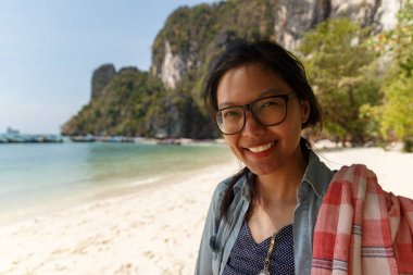 Asyalı kadınlar kumsaldaki kameraya doğru gülümsüyor.