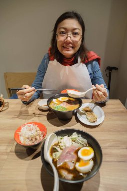 Masadaki diğer yiyeceklerle Japon eriştesi yiyen Asyalı kadın.