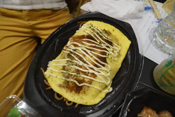 Siyah plastik tabakta soslu pilav üzerine omlet.