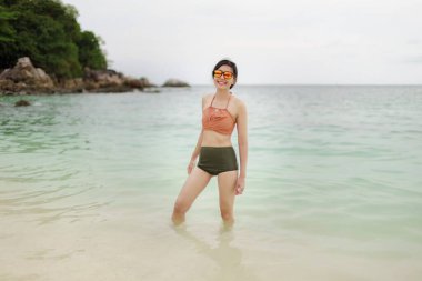 Sahilde bikinili Asyalı kadınlar yürüyor.