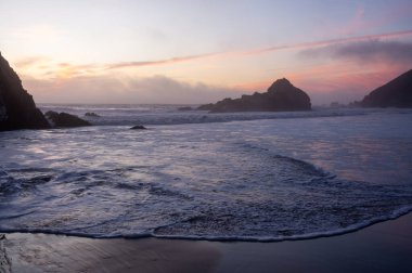 Pfeiffer sahilinde gelgit dalgaları süzülürken, gün batımının saf renkleriyle örtülüdür..