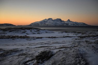 Landscape shot highlighting the rugged mountains and snow-covered beaches of arctic norway during a brief golden hour during the long winters.