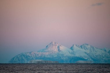Landscape shot highlighting the rugged mountains and snow-covered beaches of arctic norway during a brief golden hour during the long winters.